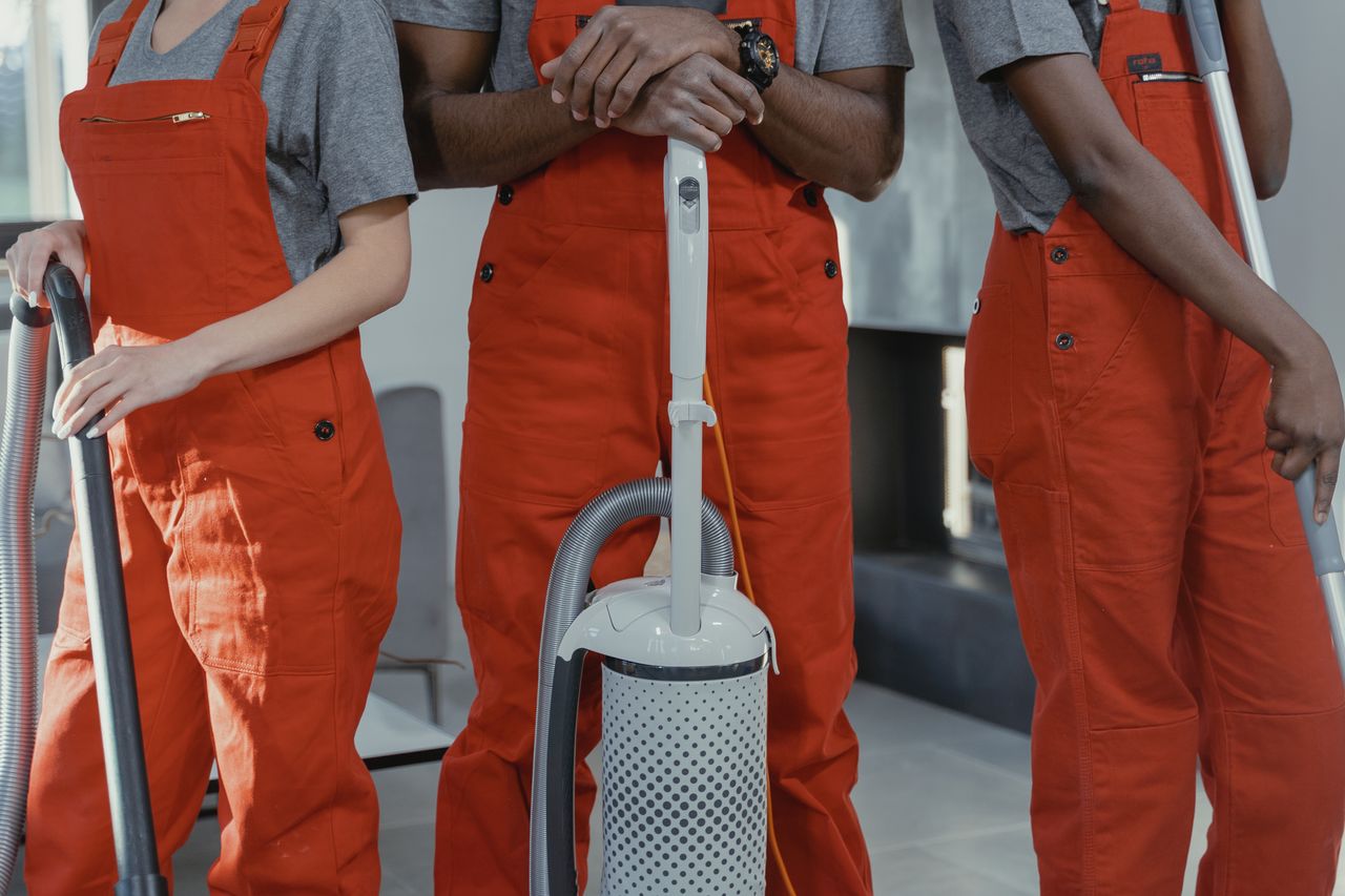 Three workers in red coveralls standing in a room with cleaning tools.